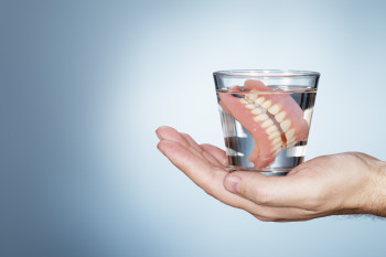 Man holding a glass containing dentures.